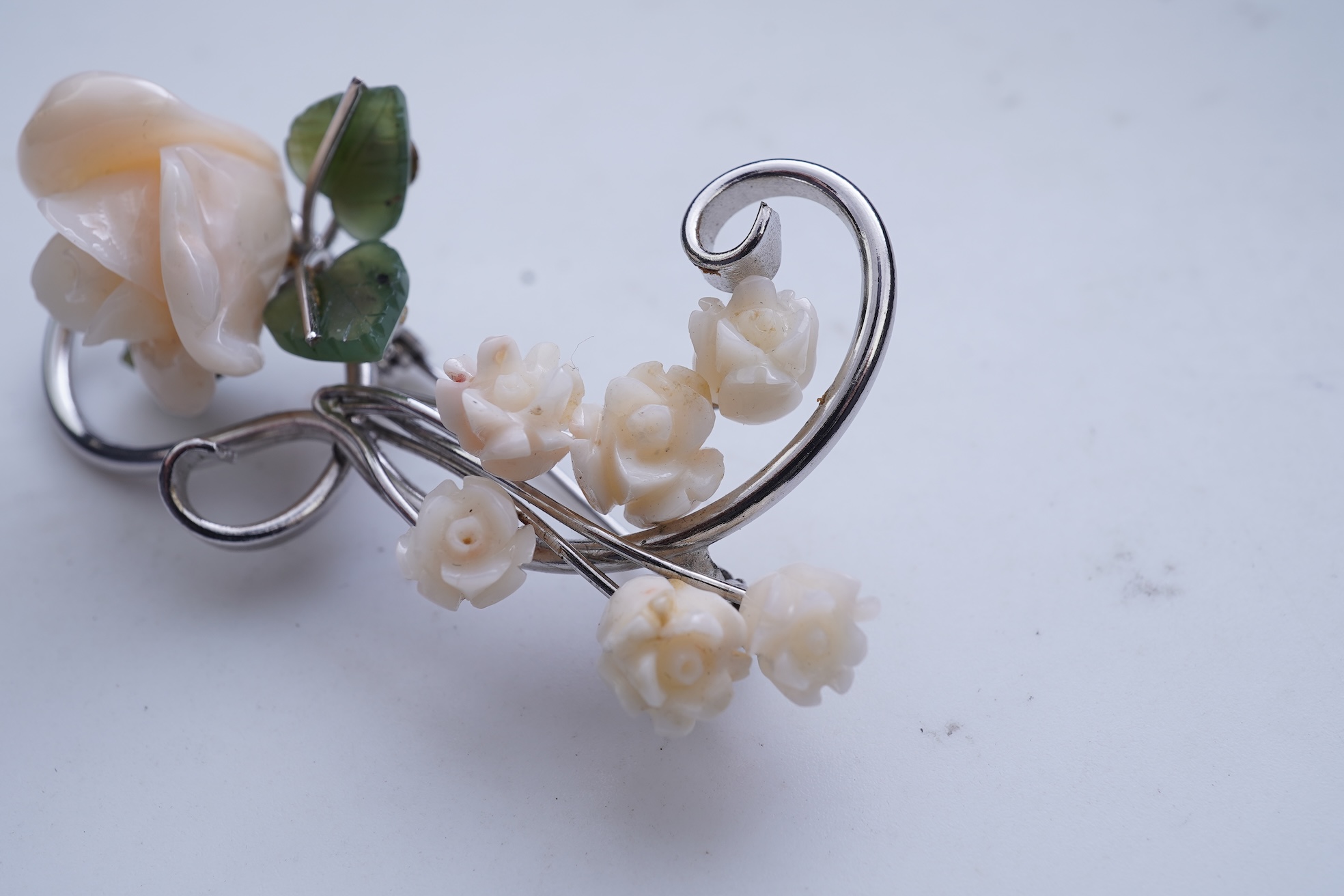 A white coral and nephrite brooch, designed as a spray of roses in carved white coral with nephrite leaves, on a scrolled white gold mount, length 5.5cm, stamped 14K, gross weight 11 grams